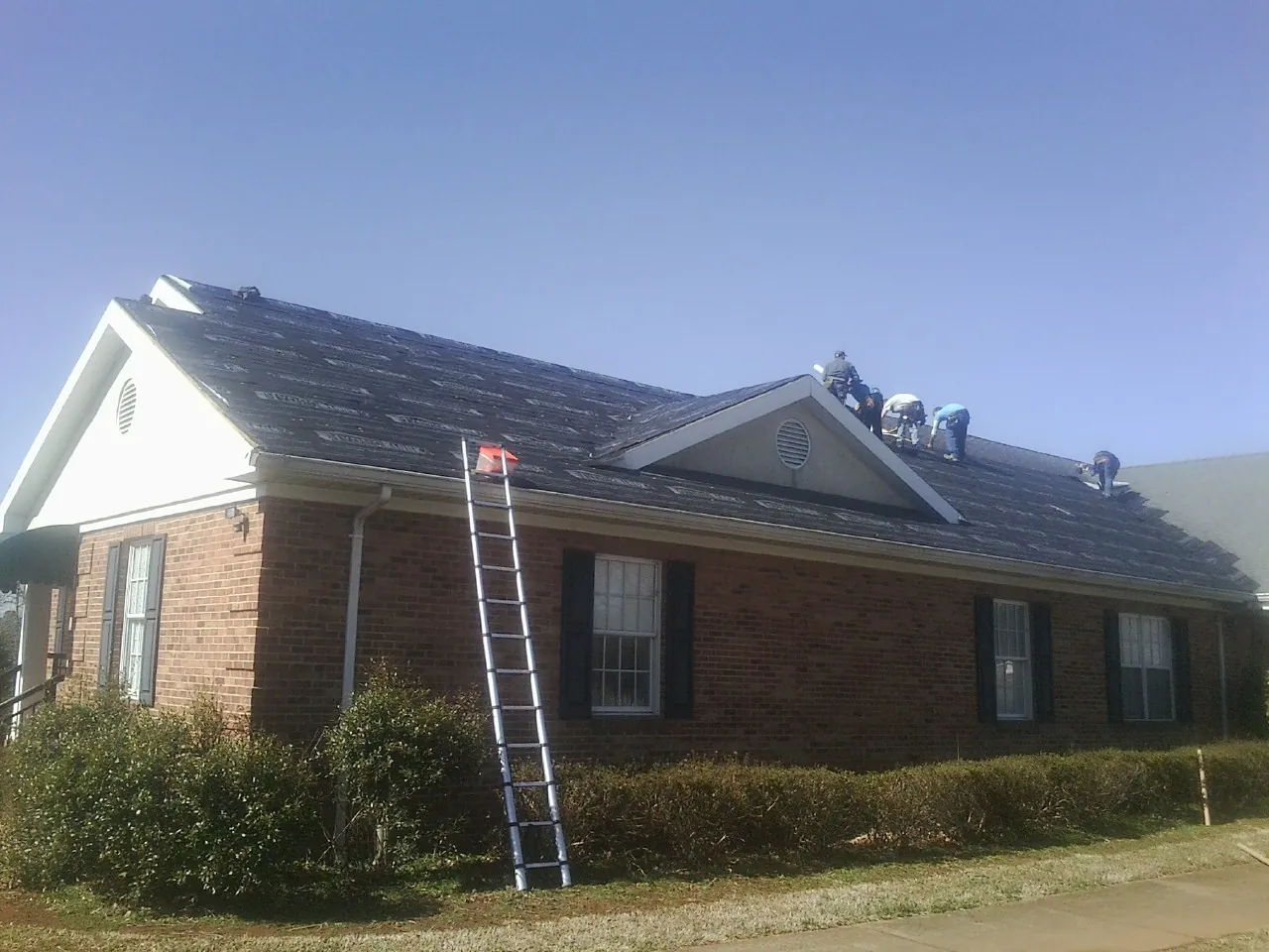 Crew tearing shingles off a brick ranch roof with a ladder set — Metal Roof Repair work by our crew in Lincolnville