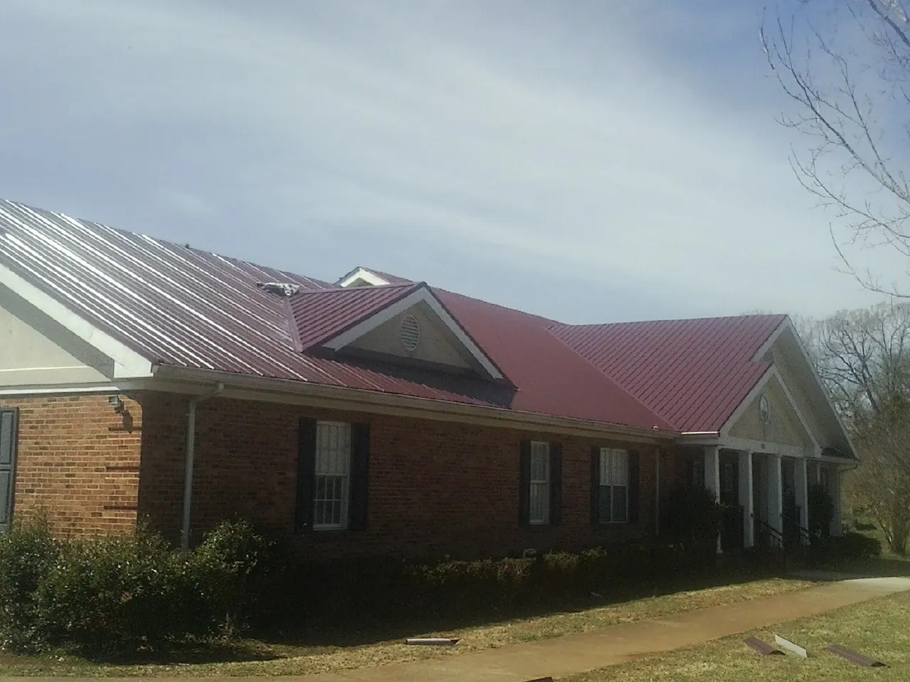 Red metal roof with gabled entries on a long brick building, from a Hail Damage Roof Repair job in Lincolnville