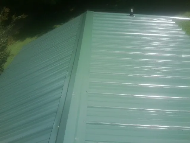 New green metal panels meeting at the ridge of a roof — Flat Roof Repair work by our crew in Lincolnville