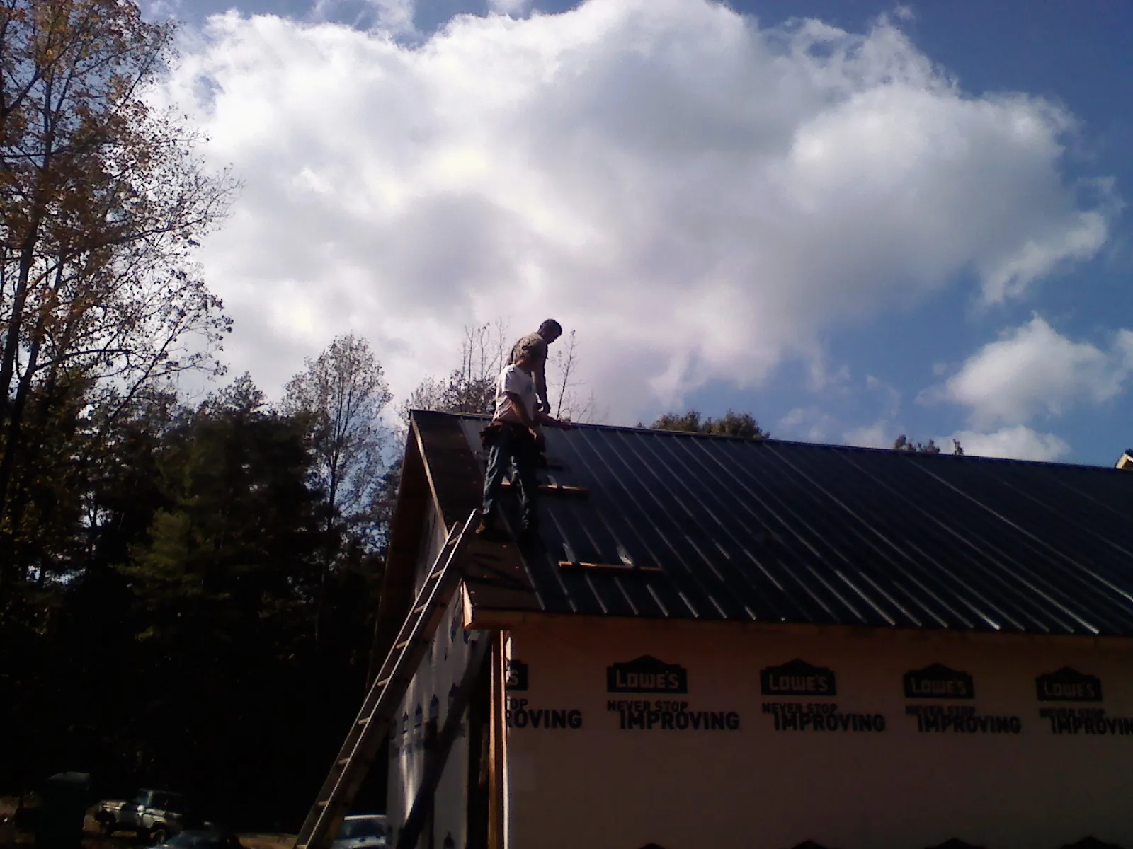 Roofer fastening dark metal panels high against a cloudy sky, from a Roof Inspection job in Lincolnville