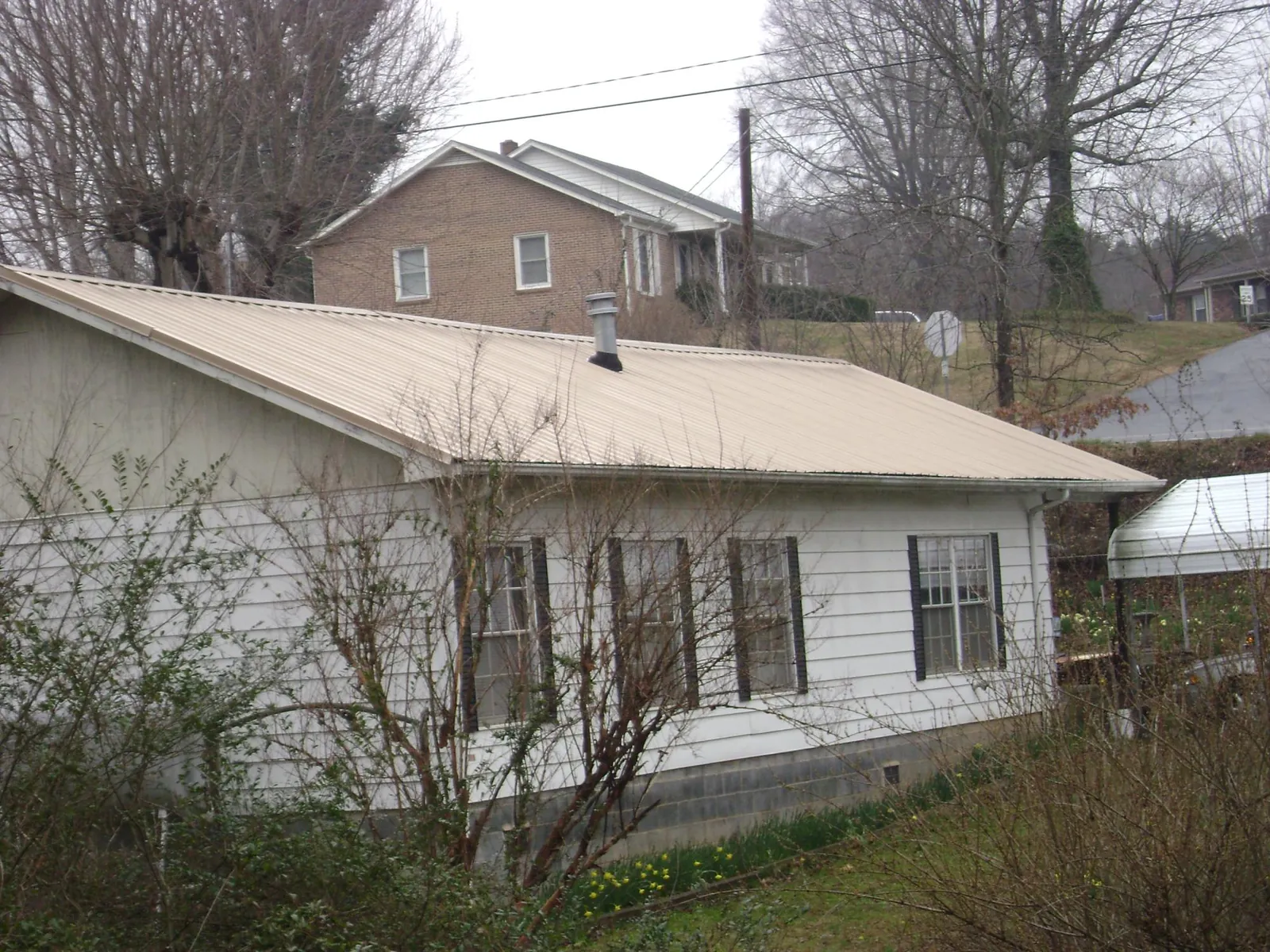 Tan metal roof on a white sided house set into a hillside — Commercial Roofing by Roofing Brothers in Lincolnville