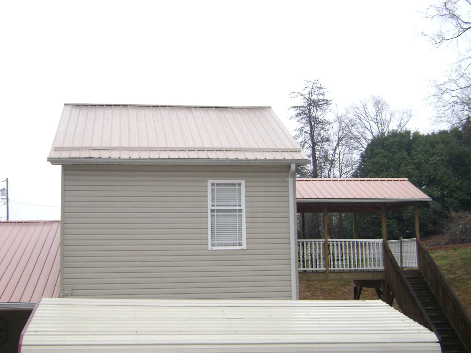 Tan metal roofs on a two story addition and attached porch, from a Roof Replacement job in Lincolnville